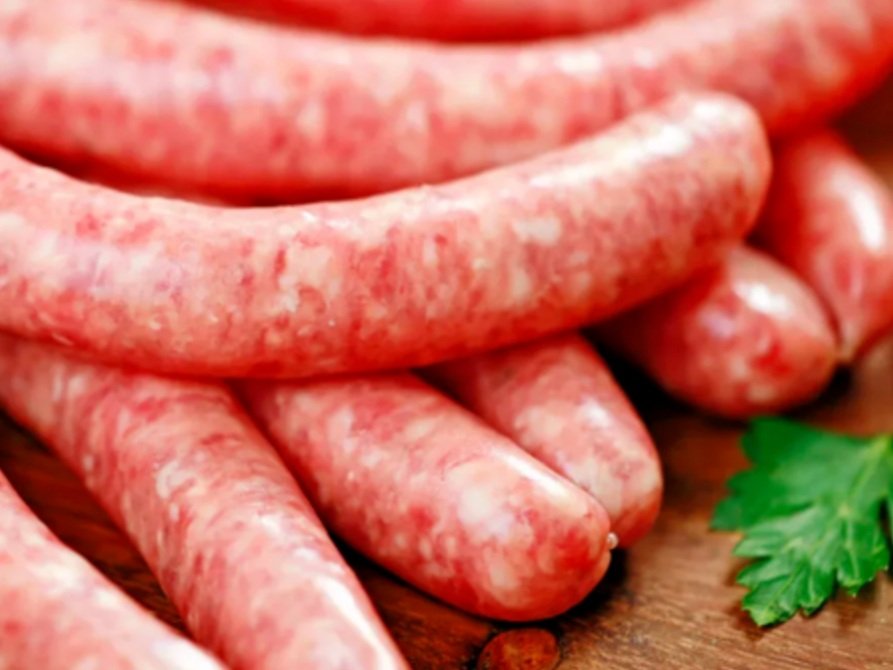 Fresh raw sausages piled on a wooden surface, showcasing a textured pink meat with visible fat, ideal for grilling or cooking in various dishes.