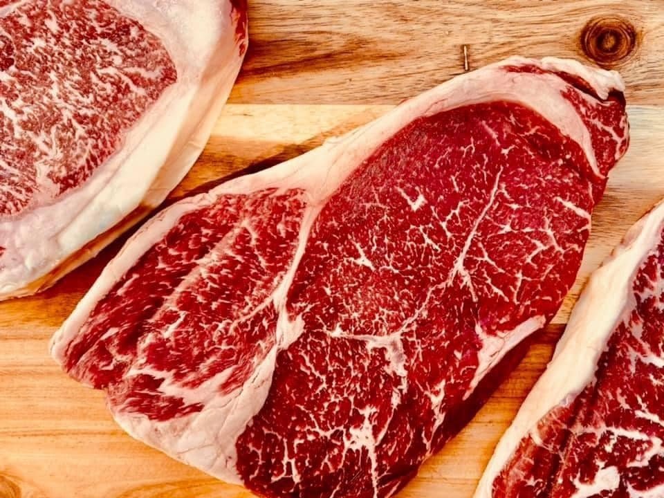 Close-up of marbled beef steaks on a wooden cutting board, showcasing rich red meat with white fat streaks, ideal for grilling or roasting.